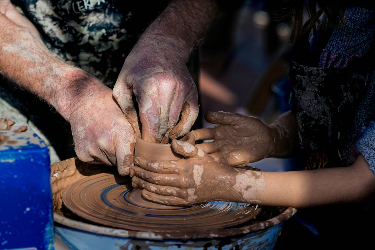 Las manos de un maestro artesano guiando las de un niño para dar forma al barro.