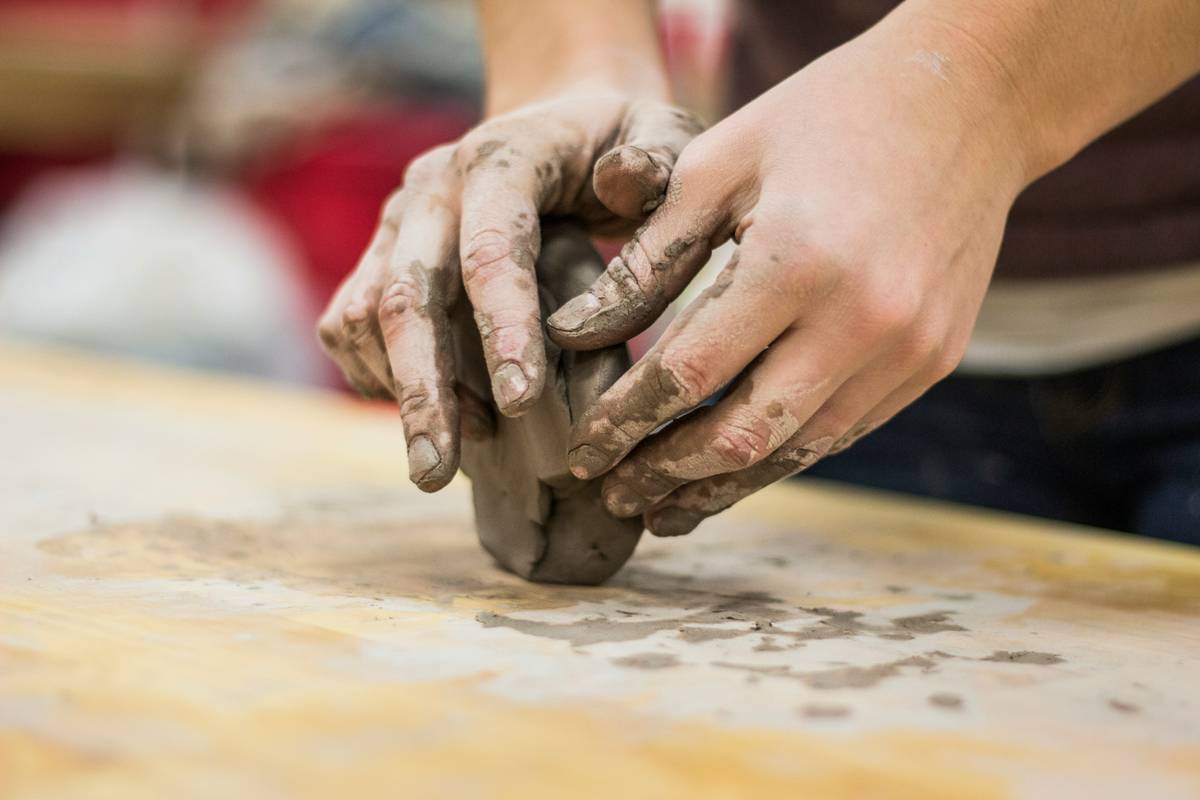 Hands centering lump of clay on pottery wheel with bag of pottery clay supplies nearby